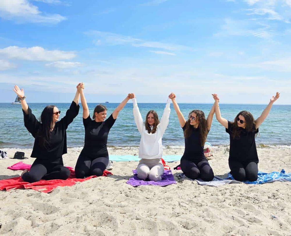 JGA Yoga Ostsee - Junggesellinnenabschied am Strand mit Freundinnen. 5 Frauen am Ostsee Strand, die sich an den Händen halten