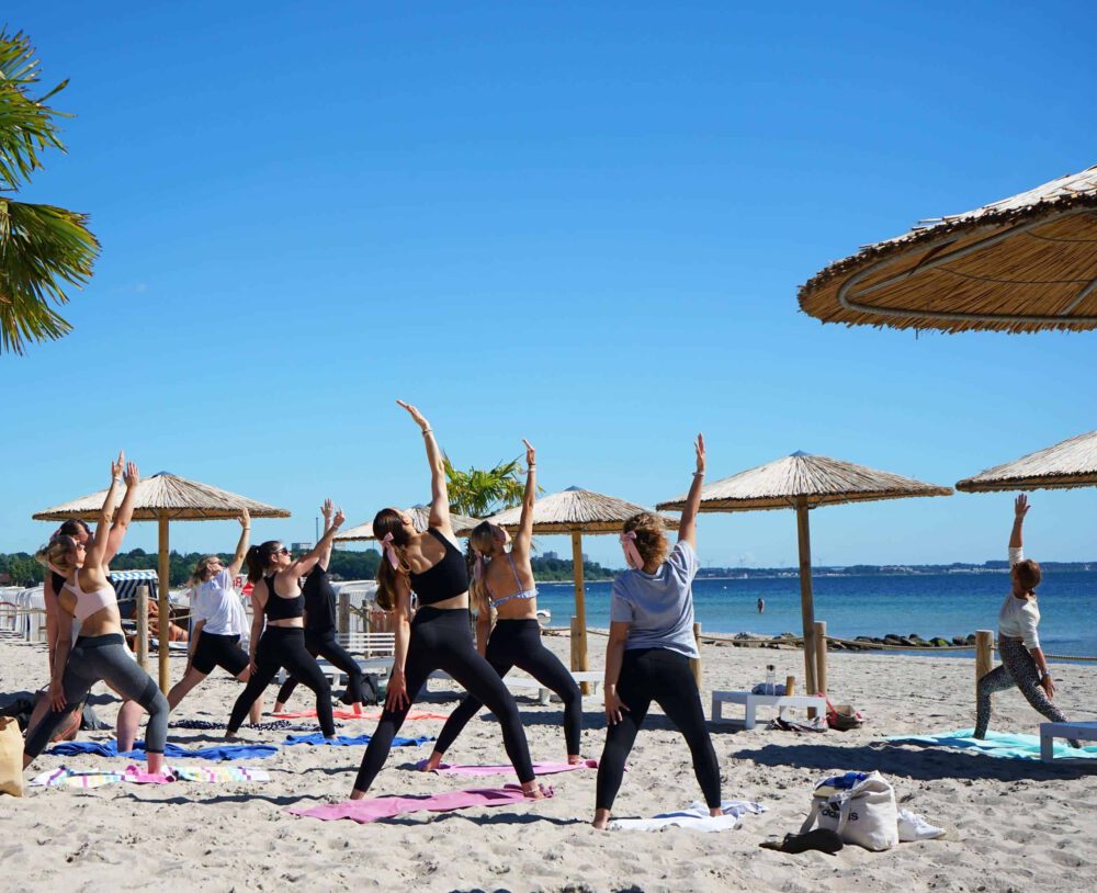 OM The Beach - Yoga Teilnehmer am Strand in Scharbeutz, Haffkrug mit Strandschirmen.