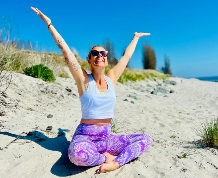 Yoga Lehrerin im Lotussitz mit ausgestreckten Armen am Ostsee Strand