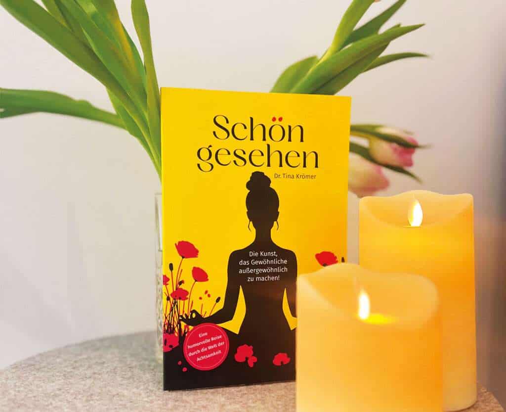 Mein kleines Buch über Achtsamkeit. Gelbes Buch und Kerzen vor einem Blumenstrauß.