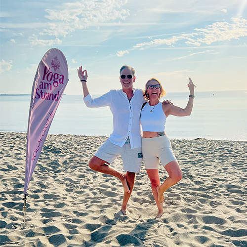 Yogacoast - Yoga an der Ostsee am Sandstrand neben einer YOGACOAST Fahne.