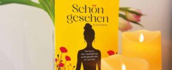 Mein kleines Buch über Achtsamkeit. Gelbes Buch und Kerzen vor einem Blumenstrauß.
