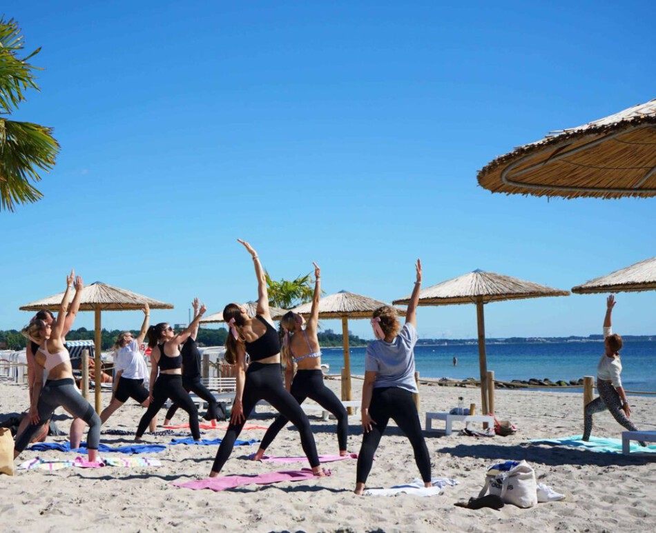 OM The Beach - Yoga Teilnehmer am Strand in Scharbeutz, Haffkrug mit Strandschirmen.