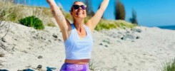 Yoga Lehrerin im Lotussitz mit ausgestreckten Armen am Ostsee Strand