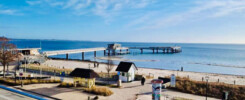 Aussicht von Balkon des Apartments strandallee.net auf die Seebrücke, den Ostseestrand und das Meer in Scharbeutz Haffkrug bei blauem Himmel.